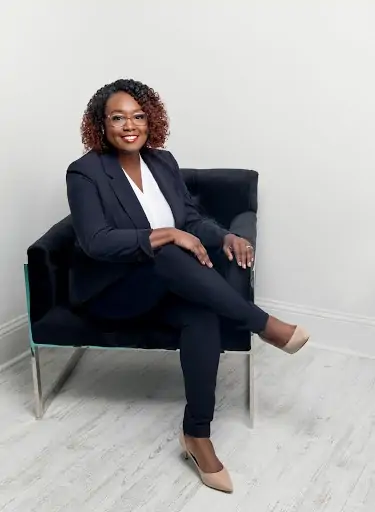 Virtual Image Consulting Client Lianne In a Blue Suite White Button Down And Nude Heels Seated On A Blue Chair