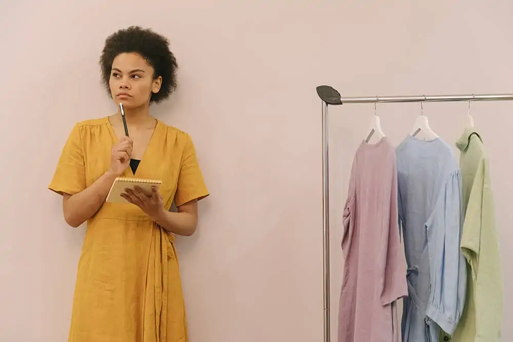 Woman Standing Next To Clothes Rack Thinking About Building A Personal Brand